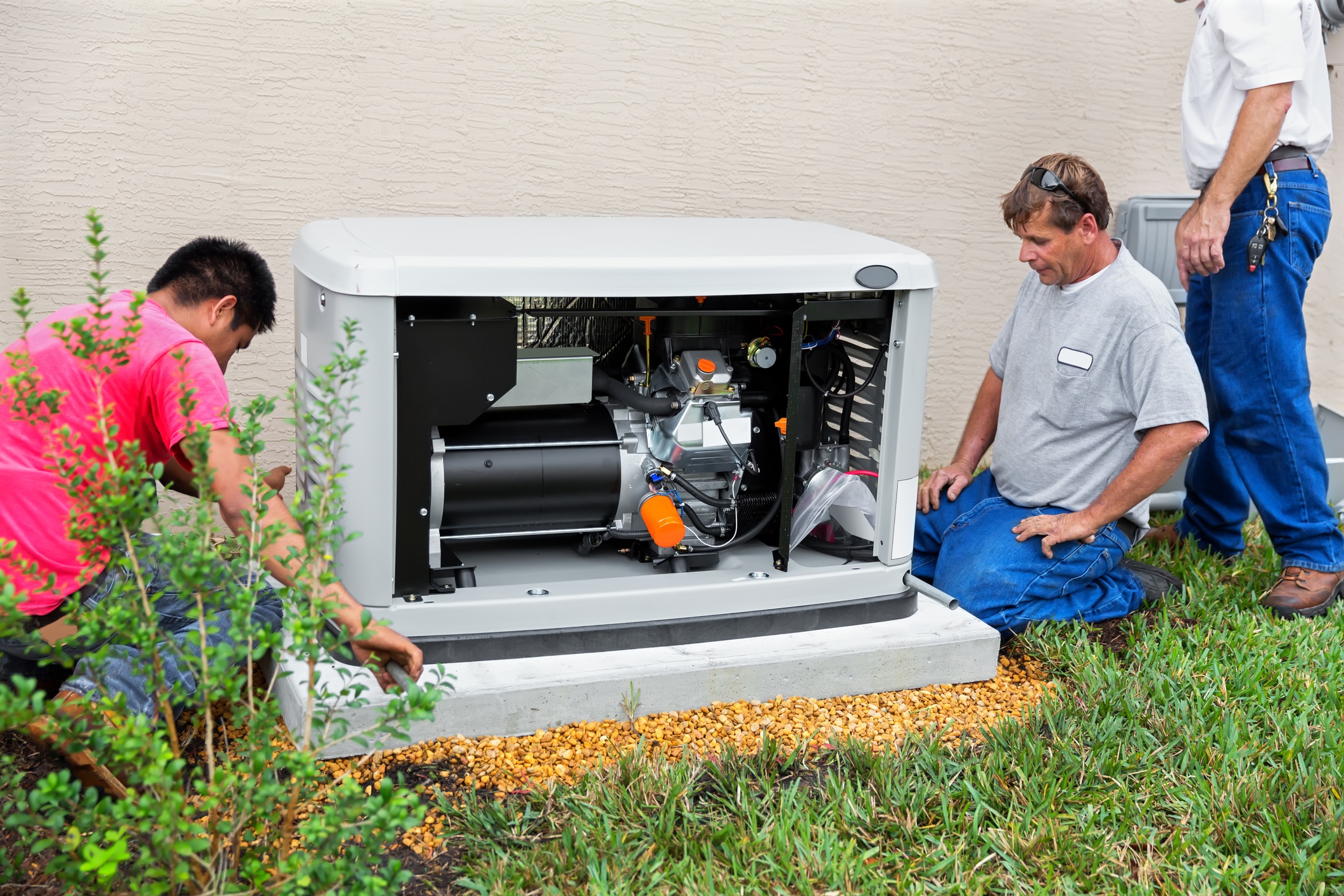 A man in a pink shirt and an older man in a gray shirt are on either side of a generator in a gray covering